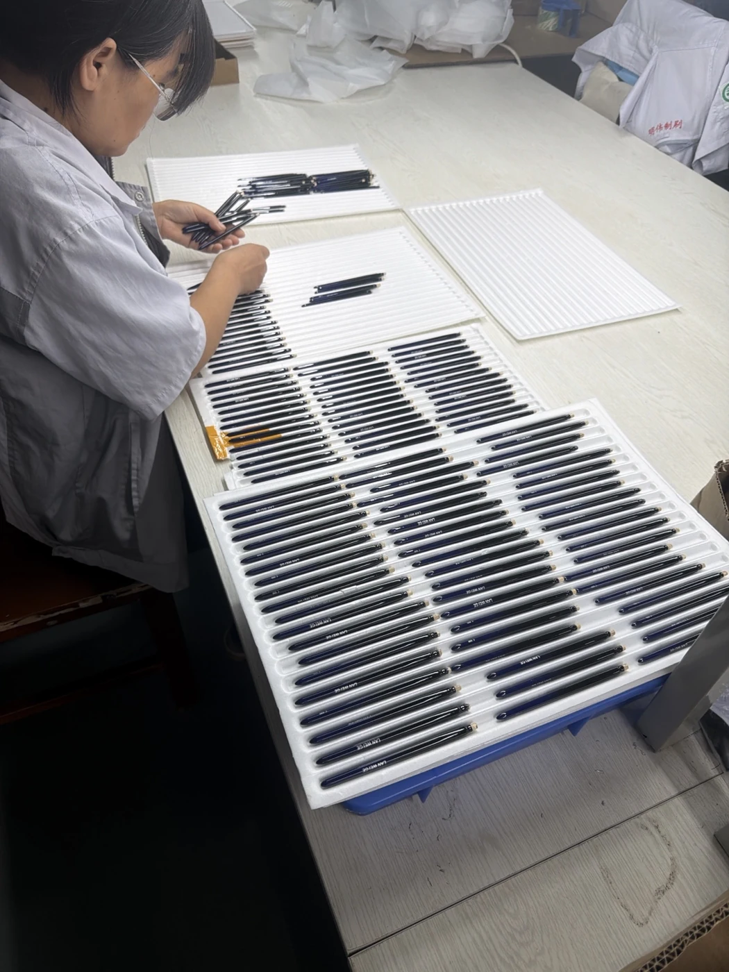 Brush handles arranged in trays beside an operator at a manufacturing workbench