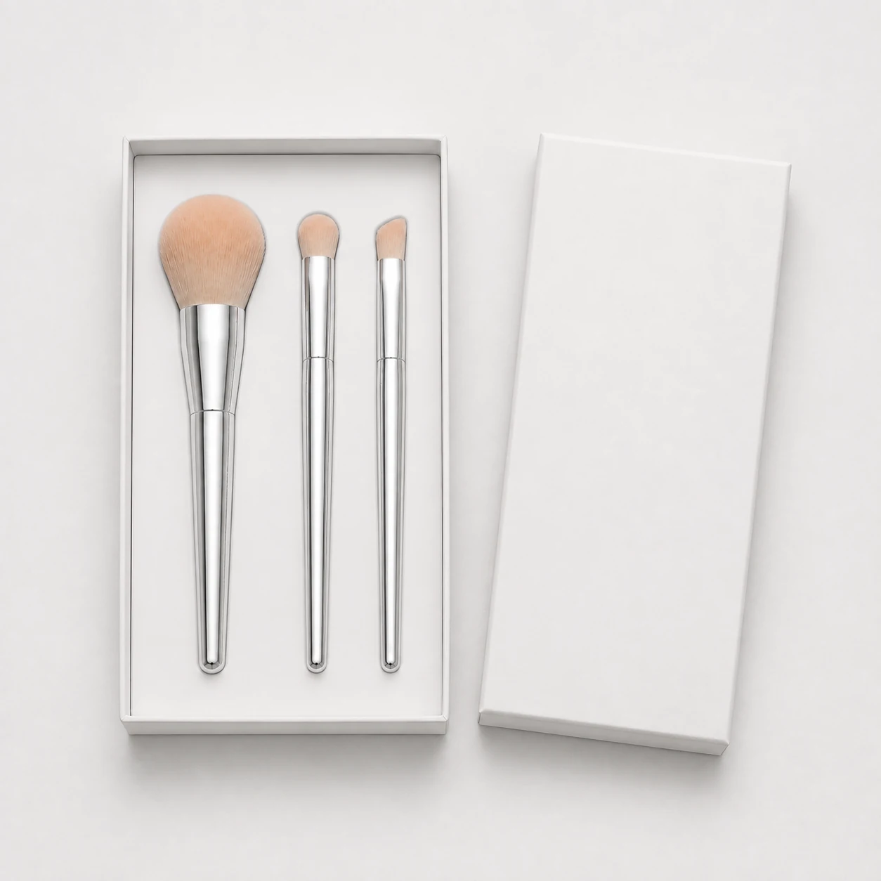 Three silver brushes in an open soft-white presentation box, a packaging design concept