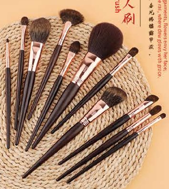 Complete eleven-brush group on woven mat - Dark tapered handles, rose-gold-tone ferrules, brown heads
